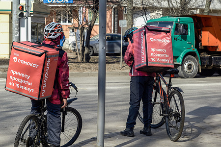 Two food delivery men on bicycles on the street of Voronezh in early spring. With the beginning of spring, warming came to Voronezh.