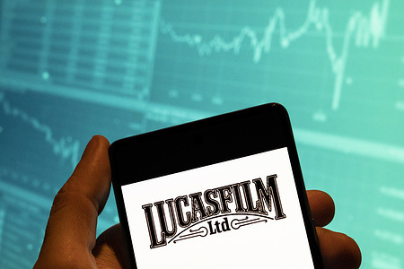 In this photo illustration, the American film and television production and label owned by Disney, the Lucasfilm Ltd logo is seen displayed on a smartphone with an economic stock exchange index graph in the background.