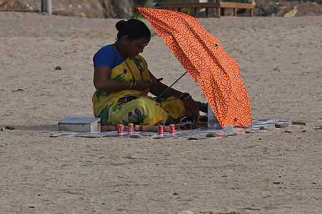 A woman shelters herself with an umbrella from the harsh sun as she checks her mobile phone in Mumbai. The city has been reeling under a heat wave in the month of March itself which is the beginning of summer.