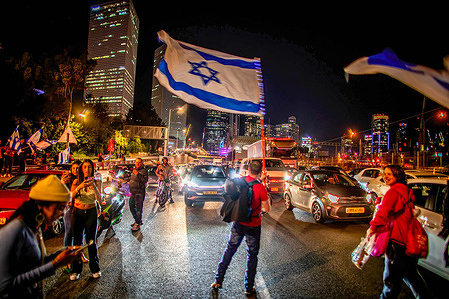 A protester waves the Israeli flag as he blocks traffic on the Ayalon High way during an anti Judicial reform night protest. Israeli protesters held demonstration against a contentious government plan to overhaul the judiciary, pushing back against Prime Minister Benjamin Netanyahu after he rejected a compromise proposal that was meant to defuse the crisis.