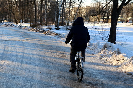 A man rides a bicycle on a snow-covered road in the Central Park of Culture and Leisure (Yelagin Park) in Saint Petersburg.