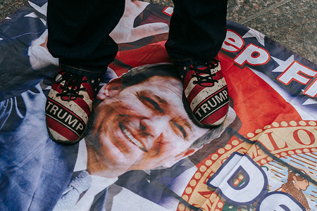 Man in Trump sneakers steps on a flag emblazoned with the face of Florida Governor Ron DeSantis, a likely contender in the 2024 presidential elections. A small contingent of supporters of former President Donald Trump gathered outside of the Trump Tower on Fifth Avenue during the annual St. Patrick's Day parade in New York City.