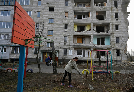 A woman clears dry leaves from a playground near a residential building damaged by shelling by the Russian army in the city of Borodyanka, Kyiv region.