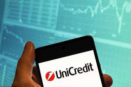 In this photo illustration, the Unicredit logo seen displayed on a smartphone with an economic stock exchange index graph in the background.