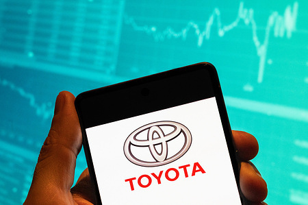 In this photo illustration, the Japanese multinational automobile manufacturer Toyota Motor logo seen displayed on a smartphone with an economic stock exchange index graph in the background.