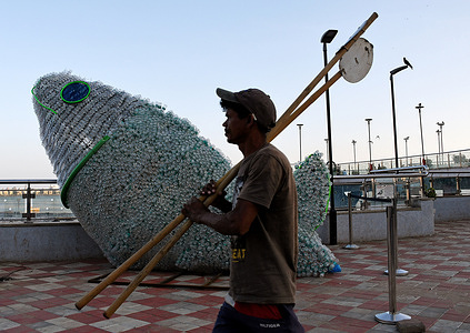 A man carrying oars walks past the PET (Polyethylene terephthalate) bottle fish installation in Mumbai. Young volunteers from Change Is Us created a PET (Polyethylene terephthalate) bottle fish to create awareness about recycling. More than six thousand plastic bottles were reused to create this gigantic installation. According to a study, by 2050 there will be more plastic than fish in the sea.