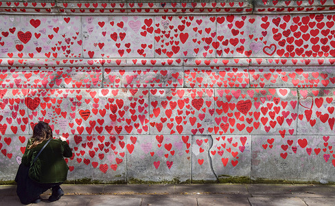 A woman writes a tribute on the National Covid-19 Memorial Wall on the third anniversary of the first national coronavirus lockdown. Over 150,000 red hearts have been painted on the wall outside St Thomas' Hospital, one for each life lost to Covid-19.