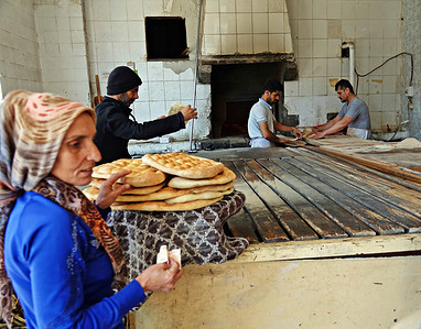 A woman is seen taking the baked bread from the oven. She made the dough at home and baked it in a bakery's oven. The tradition of baking doughnuts before the month of Ramadan and Eid al-Fitr continues in the historical city of Diyarbakir in Turkey. Some families bake doughnuts at home, while some buy them from bakeries that bake doughnuts. Special breads are also baked for the month of Ramadan. Some families also traditionally take the dough they prepare at home to a bakery's oven and bake bread.