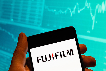 In this photo illustration, the Japanese multinational photography and imaging company Fujifilm logo seen displayed on a smartphone with an economic stock exchange index graph in the background.