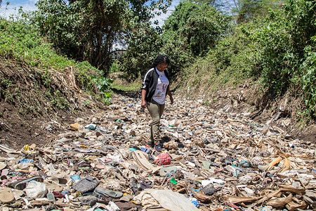A woman walks on a dry river bed littered with piles of trash, mostly plastic at Njoro River. Despite increased voluntary initiatives and national regulations to curb pollution, the problem of plastic waste ending up in the natural environment is not reducing.