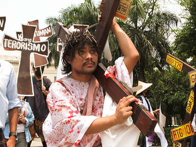 A protester acting as Jesus Christ is carrying a cross during the play. Militant protesters staged a demonstration with their own version of the "Passion of Jesus" play at the Liwasang Bonifacio in Manila in time of Holy Week. Protesters dramatize it by symbolizing the suffering or the Calvary of every Filipino people, calling for wage hikes, ending job contractualization, and landlessness of Filipino farmers, and crying for justice for victims of Martial Law.