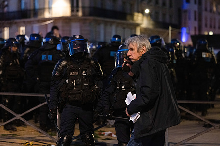 A civilian is seen walking past in front of the riot police at a scene of riot in central Paris. Protesters lingered and caused riots after the biggest general strike yet in France as President Macron pushed through his pension reform plan without voting by the Parliament to raise the retirement ages from 62 to 64.