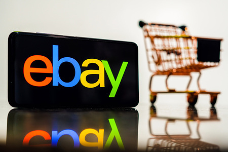 In this photo illustration, the eBay logo seen displayed on a smartphone along with a shopping cart.