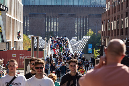 Tourists walk across the Millenium Bridge on a sunny day in front of the Tate Modern Gallery.