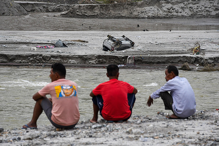 Three men watch an overturned car seen along the Teesta River after flash floods caused by a lake burst. A glacial lake in northeast India burst through a dam shortly after midnight, washing away homes and bridges and forcing thousands to flee.