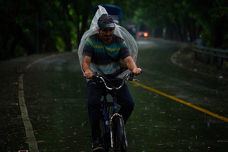 A man riding a bike while sheltering himself under with plastic during the onset of Storm Pilar. El Salvadoran government released a national state of emergency due to Storm Pilar. According to the US National Hurricane Center, Storm Pilar brought heavy rains to EL Salvador. They informed the public that heavy rains would produce flash and urban flooding and mudslides in higher terrain areas.
