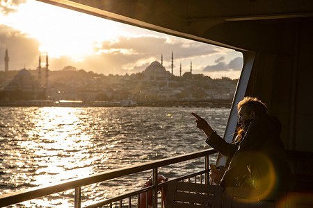 Passengers from the city lines ferry and the silhouette of the Suleymaniye Mosque in the background seen during sunset in Istanbul.