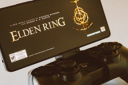 In this photo illustration, the Elden Ring logo is displayed on a smartphone screen, next to a gamepad. Billionaire Elon Musk recently said that he calms his mind by playing this video game.