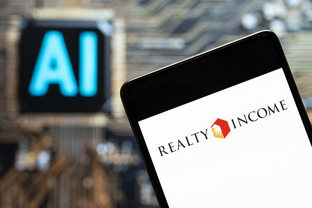 In this photo illustration, the real estate investment trust Realty Income Corporation (NYSE: O) logo seen displayed on a smartphone with an Artificial intelligence (AI) chip and symbol in the background.