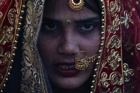 A Nepalese Hindu woman looks on with jewelleries on her face while offering prayers to the setting sun on the banks of the Bagmati river during the Chhath festival in Kathmandu. On the day of Chhath, an ancient festival observed by Hindus, devotees gather by the holy river to offer prayers by fasting, bathing, and standing in the water for continuous periods to offer prayers to the Sun God, thanking and paying respects to seek blessings for sustaining life on earth.