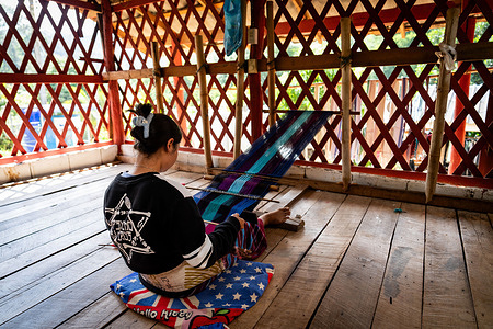 A Karen person weaves textiles at their village home near Doi Inthanon in Chiang Mai. The Thai Government pushes for growth in the international tourism market, recently enacting visa-free entry programs to the Kingdom for international tourists from Russia, China, and India.