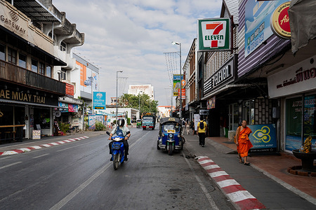 A general view of 7-Eleven, a monk, a tuk tuk, and a motorcyclist downtown Chiang Mai, Thailand.
