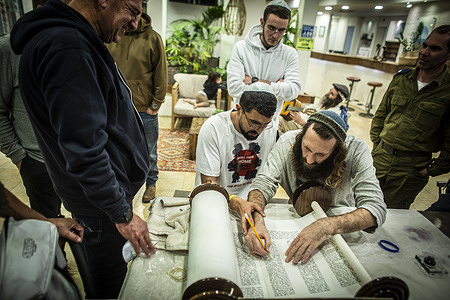 A member of the Kfar Aza kibbutz community (L) sits next to a volunteer writing a Bible Scroll in honor of the Israeli hostages held by Hamas in Gaza at their refuge shelter in kibbutz Shfaim.