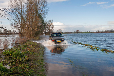 A car seen driving through a flooded road due to heavy rain and wind factor. The National Coordination Flood Threat Committee (LCO) of Rijkswaterstaat acted swiftly on Thursday due to expected high water levels along the coast, IJsselmeer, and major rivers. Storm surge barriers like the Hollandse IJsselkering in Zuid-Holland and the Haringvlietsluizen are scheduled to close on Thursday evening. Strong winds are driving water up along the coast, prompting a yellow code warning from KNMI for coastal areas on Friday.