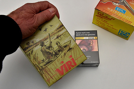 In this photo illustration, a box of hunting cartridges is held above a pack of cigarettes. Next year, tobacco shops in France will be allowed to sell Category C ammunition like shotgun shells and smoothbore cartridges due to new rules from the French Interior Ministry. For tobacco shops interested in selling these items, they need to complete a two-day training course approved by the Professional Federation for Careers in Weapons and Munitions (FEPAM).