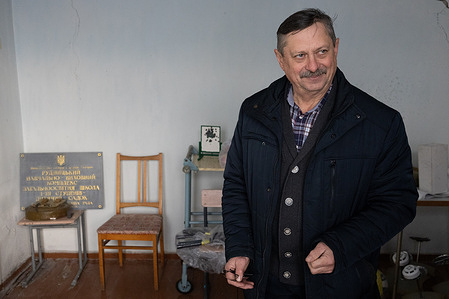 Director of a rural school destroyed during the Russian invasion in the spring of 2022 answers media questions, in the background a surviving sign with the name and number of the burnt school in the village of Rudnytske, Kyiv region.