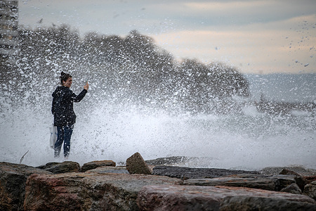 A woman seen standing on the rocks on the beach taking photos of the high waves. Due to the southwest wind affecting Istanbul, high waves were seen on the Moda coast.