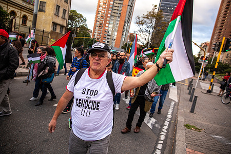 A protester wearing a T-shirt that says "Stop the Genocide" seen waving a flag during the demonstration. March in Bogotá for the International Day of Solidarity with the Palestinian People.