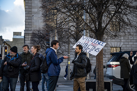 A protester holds a placard reading "Violence is not Dublin's voice" as he is interviewed. On 23 November 2023, Dublin experienced one of the most serious riots in its history since independence. Following the attempted stabbing of three children in front of a school in the city centre, the Irish far-right leaders called out their followers on O'Connell street, Dublin's central thoroughfare, to violently protest against immigrants and the country's reception policies. The violent riots forced some looted shops to close for days.