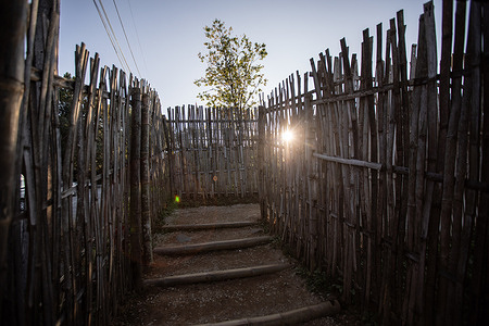 Narrow pathway surrounded by high bamboo fences to enter the Chang Moob Military Outpost as sun shine through. The Chang Moob Military Outpost now turned into a tourist attraction spot, used to be a Thai Royal Army location to prevent drug smuggling and keep an eye on other suspicious activities on the Myanmar side (mostly in the 1990s). Also called the "Doi Tung Trenches" It starts off with a narrow pathway through high bamboo fences before reaching the main spot with deep trenches along the northernmost sections of the Thai-Myanmar border, with a stunning view of Myanmar mountains.