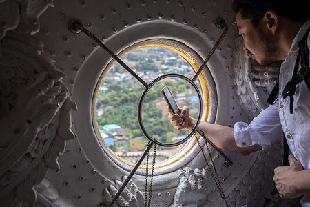 A tourist takes a photo from the window of Guanyin bindi from inside the Guanyin statue. The "Wat Huay Pla Kang", also known as “Big Buddha of Chiang Rai”, is well known for its enormous white statue of Guanyin (In Chinese Mythology, The Goddess of Mercy). The recently built temple is a mix of Thai Lanna and Chinese styles located on a hill in the rural area North of Chiang Rai town.
