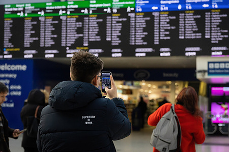 A commuter takes a phone picture of digital train timings at Waterloo Station in London. Flights and trains have been cancelled, and "danger to life" warnings remain in place with a risk of possible tornadoes in parts of the country due to Storm Isha.