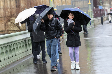 People on Westminster Bridge in central London shelter under umbrellas during the rainfall in the capital.