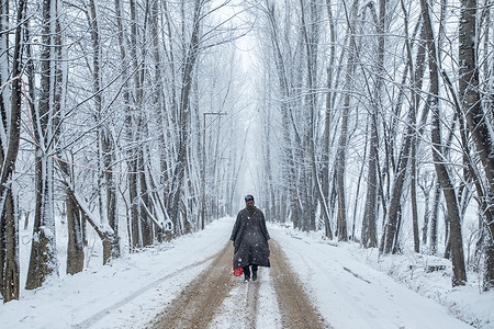 A Kashmiri man walks along a snow-covered road amid fresh snowfall in Srinagar. Several parts of Kashmir, including Srinagar city, received fresh snowfall on Saturday as the weather department predicted moderate to heavy snowfall in the valley over the next 48 hours. Moreover authorities have issued avalanche warnings in hilly and mountainous areas of the region.