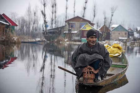 A man seen touching a Fire pot (Kangri) on his boat during snowfall. The plains of Kashmir are witnessing moderate snowfall while heavy snowfall has been reported in the higher reaches of the valley. The Kashmir valley received a fresh snowfall which disrupted the normal life of people. Flight operations, surface transport, and routine activities of life came to a grinding halt.