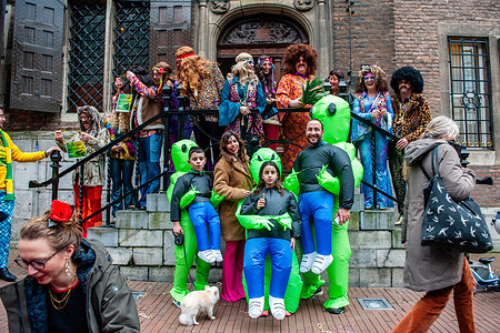A family wearing funny costumes is seen taking a photo with Huber Bruls (orange costume) during the event. In Nijmegen, The Netherlands the carnival parade consists of one float pulled by an electric vehicle full of the princes and princesses of the year. The rest of the parade consists of people dressed up in colorful costumes and music bands. The main attraction each year is the costume that the Mayor of the city Huber Bruls will be wearing, this year the theme was Flower Power.