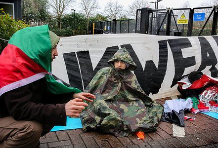 A supporter wearing a Palestinian flag as a cape talks to one protester while they block the road. Supporters of Palestine Action use lock-ons to blockade the only vehicular access to Israeli defence company, Elbit Systems’s business in Aztec West, Bristol. They argue that weapons made by Elbit in the UK are being used by the Israel Defence Force against Palestinians in Gaza and elsewhere. Israeli bombing in Gaza has killed over 30,000 Palestinians since October 2023. Palestine Action are determined to relentlessly target Elbit and their partner companies by direct action and make business for them in the UK impossible.