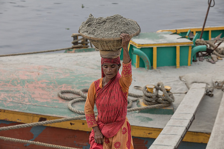 A woman works as a day laborer to off load sand from the barge at a local sand market. In recent times for the urban development sand demanded is very high and it's going on everyday. To meet the demands, sand has to come on barges from various locations, to the capital of Dhaka's biggest sand market 'Gabtoli Sand Market'.