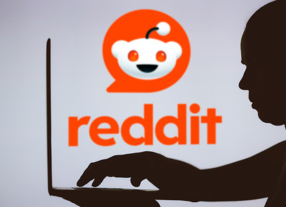 In this photo illustration, the Reddit logo is seen in the background of a silhouette of a person using a notebook.