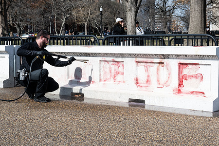 A person cleans graffiti from a pro-Gaza protest that originally said "Genocide Joe" (with only "de Joe" still visible in the image after some cleaning had already been done) off a barrier on Pennsylvania Avenue in front of the White House near Lafayette Park.