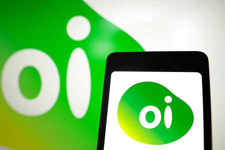 In this photo illustration, the Oi logo is displayed on a smartphone screen and in the background.