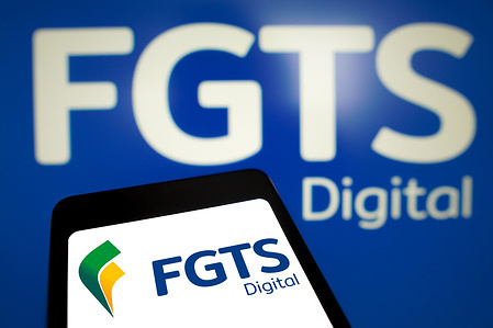In this photo illustration, the FGTS Digital logo is displayed on a smartphone screen and in the background.
