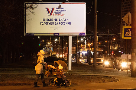 A woman with a kid stroller walks down the street under an advertising billboard informing about the presidential elections in Russia on March 15-17 with the inscription "Together we are a force - vote for Russia" in St. Petersburg.