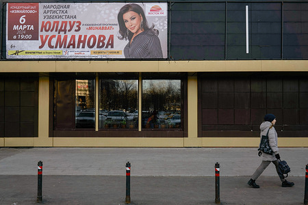 A passerby opposite a sign with Central Asian singer Yulduz Usmanova on the facade of the Izmailovo concert hall in early spring Moscow.