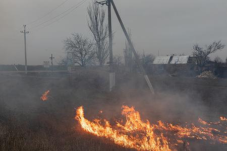 Burning grass is seen in the outskirts of a village in Mykolaiv region of Ukraine. A typical scene of a Ukrainian villages in Mykolaiv region, as in other regions of Ukraine after the occupation and near the front line. Regular shelling and destroyed houses of local residents.