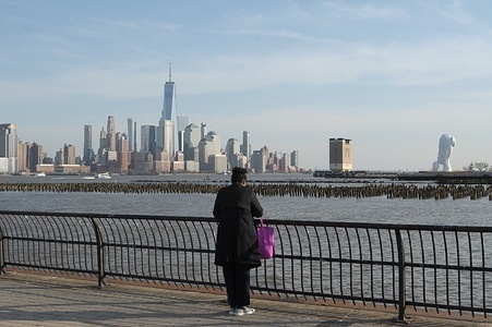 A pedestrian is seen by the Hudson River in Jersey City, New Jersey as the New York City skyline and the One World Trade Center are seen in the background.